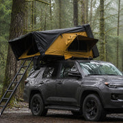 TrailNest side-opening rooftop tent mounted on an SUV during light rain at a forest campsite