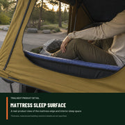 Camper seated beside the visible mattress sleep surface inside the TrailNest rooftop tent