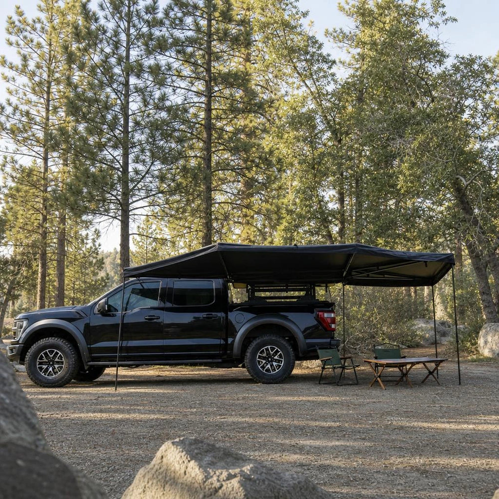 Illustrative woodland campsite with a black pickup and vehicle-mounted fan awning, based on supplier reference photo